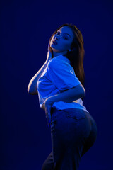 Young girl posing and moving in a black studio with colored light	