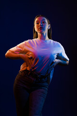 Young girl posing and moving in a black studio with colored light