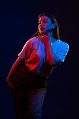 Young girl posing and moving in a black studio with colored light	