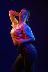 Young girl posing and moving in a black studio with colored light	