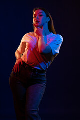 Young girl posing and moving in a black studio with colored light	