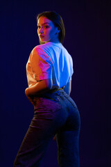 Young girl posing and moving in a black studio with colored light	