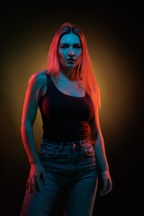 Young girl posing and moving in a black studio with colored light	