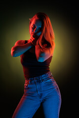 Young girl posing and moving in a black studio with colored light