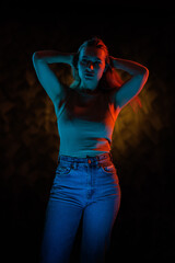 Young girl posing and moving in a black studio with colored light	