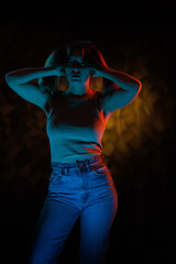 Young girl posing and moving in a black studio with colored light	
