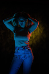 Young girl posing and moving in a black studio with colored light	