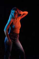 Young girl posing and moving in a black studio with colored light	