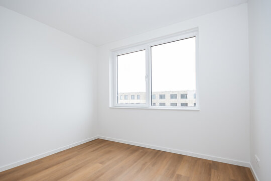interior empty basic bedroom in modern new build residential smart house. Glass window is neighboring building over the road. Plain white walls and wood effect vinyl flooring make blank canvas