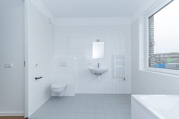 interior clean white tiled bathroom with sink, toilet WC and mirror in modern new build residential smart house through window is further development phase of project construction site building