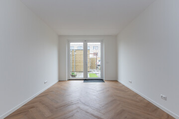 interior living room of modern new build residential smart house looking through glass patio door window at basic back garden plot with wooden shed. Brand new property freshly handed over to new owner