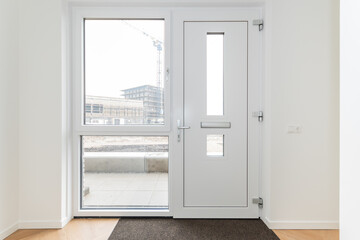 interior reception room of modern new build residential smart house looking through glass front door window at further development phase of project construction site building in scaffolding and crane