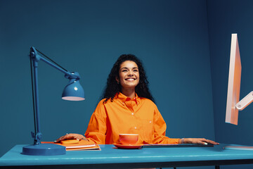 Confident young female creative smiling and sitting at desk in studio shot