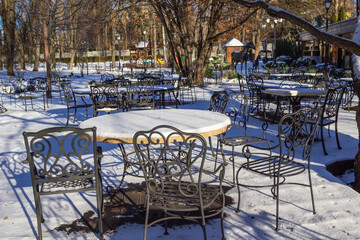 Empty winter cafe terrace. Round tables with snow and patterned metal chairs