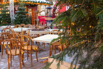 Outdoor terrace of a winter cafe. Empty wooden tables and chairs among coniferous trees