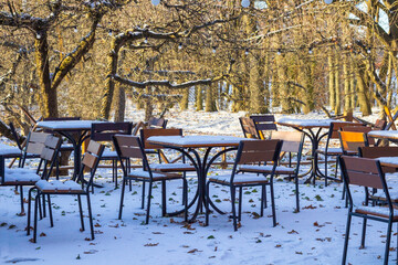 Outdoor terrace of a winter cafe. Snow-covered tables and chairs among the trees.