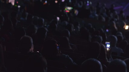 Crowded audience captured from behind while they watch live stage performance, highlighting technology use.
