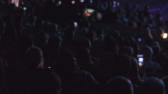 Crowded audience captured from behind while they watch live stage performance, highlighting technology use.