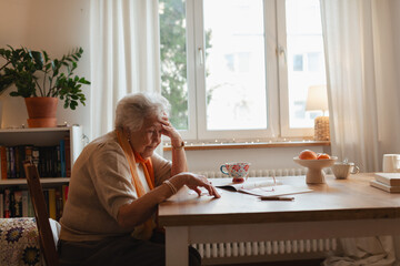 Elderly woman looking sadly at few banknotes on table. Concept of financial concerns for seniors.