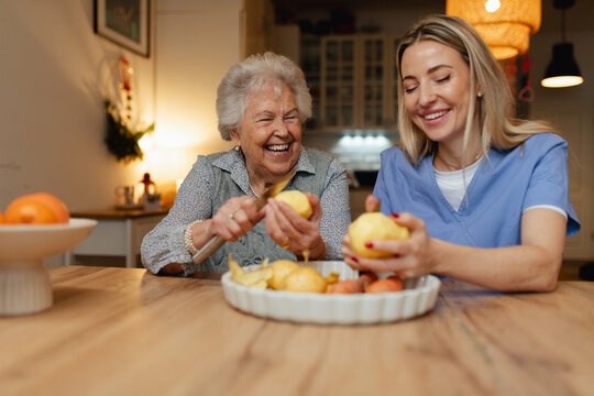 Portrait of elderly companion assistant and senior woman peeling potatoes. Home health care services.