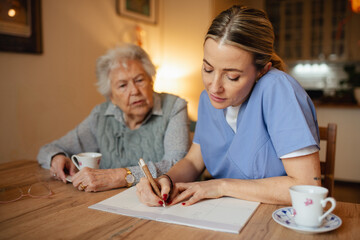 Social worker helping elderly lady with managing her finances, working on financial plan.