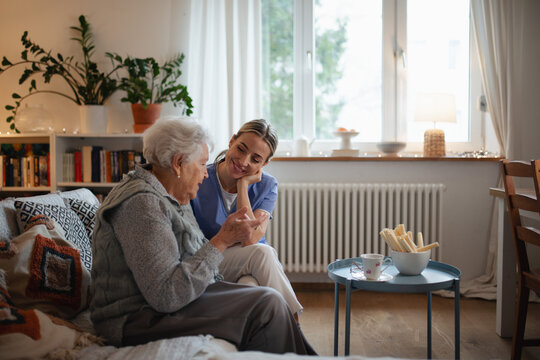 Caring healthcare worker visiting a senior patient at home, talking with her in living room.
