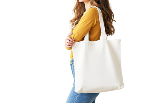 Woman in mustard shirt and jeans holding blank canvas tote bag over shoulder on white background. Ideal for branding, mockup, or product presentation. Ai generative - Powered by Adobe
