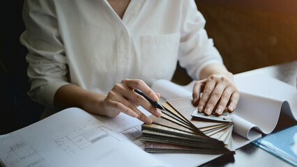 A close-up of a female architect choses colors for the interior, working at her desk in the office.