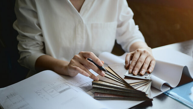 A close-up of a female architect choses colors for the interior, working at her desk in the office.