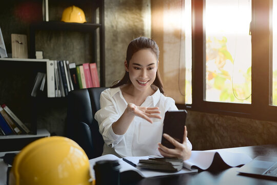 A confident, beautiful Asian female interior designer talking on a video call through her smartphone