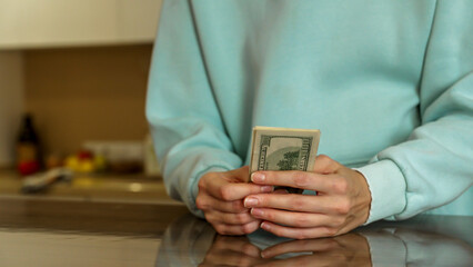 A person stands in a sleek kitchen, holding a stack of cash in both hands. The modern decor and soft lighting create a relaxed atmosphere, emphasizing the focus on the money.