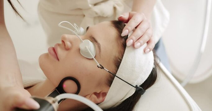 Facial rejuvenation, beauty woman with protective glasses, aesthetic medicine is performing procedure. Close up of a young girl getting laser face treatment in a medical center, skin rejuvenation