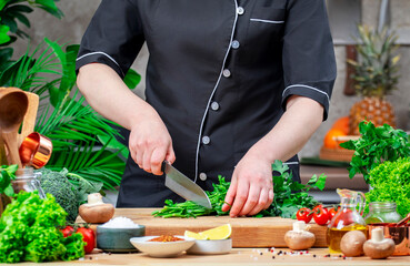 Chef cuts off the stems of parsley. Cozy kitchen with wooden table, kitchenware, vegetables, herbs and ingredients for cooking. Healthy vegan eating, culinary, recipes, blogging