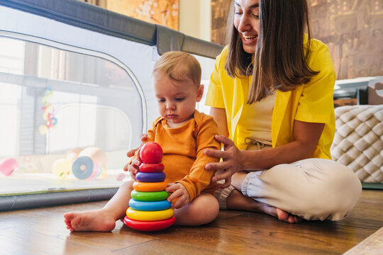 Mother sitting near son playing with plastic ring toy at home