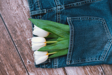 Fresh white tulips tucked in denim jeans pocket on wooden surface