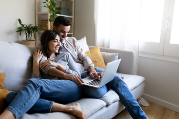 Happy couple using laptop relaxing sitting on the sofa. Copy space.