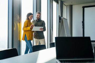 Smiling business people discussing over tablet PC near window in office