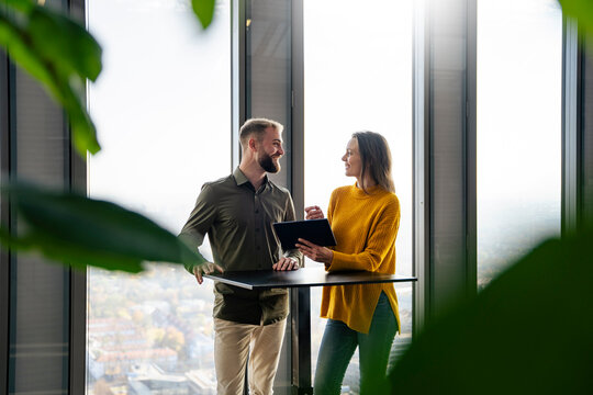 Smiling businessman discussing over tablet PC with businesswoman at table