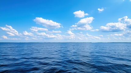 Obraz premium A serene view of the ocean under a bright blue sky dotted with fluffy white clouds, creating a peaceful and calming atmosphere.