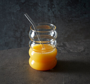 Glass cup with orange juice and glass straw in studio setting