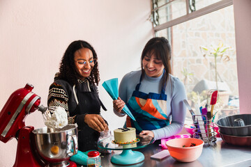 Happy woman helping friend decorating cake using icing bag at home