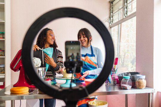 Happy multiracial friends making cake and filming tutorial through smart phone
