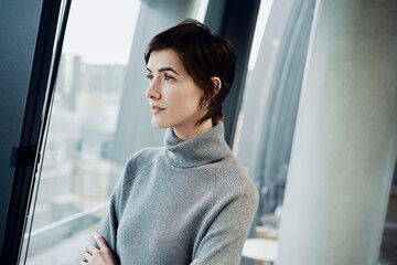 Thoughtful short haired businesswoman near window at office