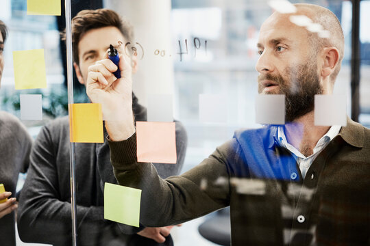 Shaved head businessman writing on glass wall at office