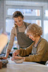 Obraz premium Two women work together with clay, developing skills and enjoying the artistic process. Elderly Caucasian woman learns pottery at a creative workshop with a young mentor