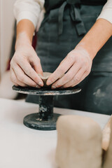 Hands shaping clay into dish in the craft studio close-up. Artisan sculpts ceramic bowl using potter's wheel.