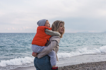 Mother carries son on her back while walking along the beach in winter