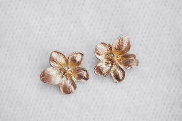 Gold flower stud earrings resting on fabric surface