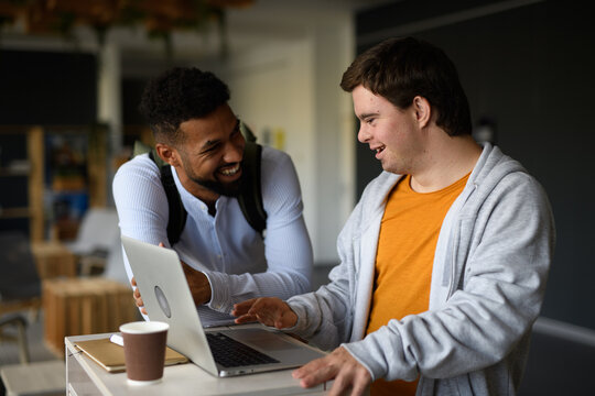 Happy young man with Down syndrome and his tutor using lapotp indoors at school.