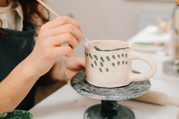 Painter is drawing and adding unique designs to the earthenware. Artist is decorating and painting handmade ceramic clay cup in the creative workshop.